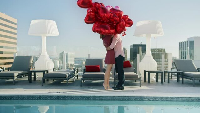 Happy young woman with red balloons walking at pool on rooftop of modern city