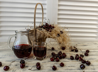Cherry and cherry juice or wine on a wooden table, a decanter and a glass with juice, a basket with...