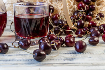 Cherry and cherry juice or wine on a wooden table, a decanter and a glass with juice, a basket with cherries