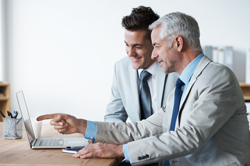 Obraz premium Hes teaching him the ropes of the business world. Two corporate businessmen looking at a laptop.