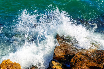 Foamy Mediterranean sea hitting rocky shore during hot summer day.