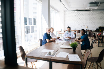 Team of multiethnic professional doctors sitting at desk in hospital office and looking at camera, discussing together history disease of patient during medical conference.