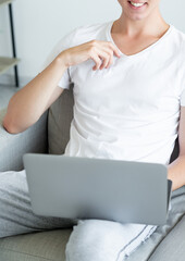 Naklejka premium Virtual meeting. Casual man. Online conference. Happy unrecognizable guy sitting sofa with laptop holding on knees light room interior.