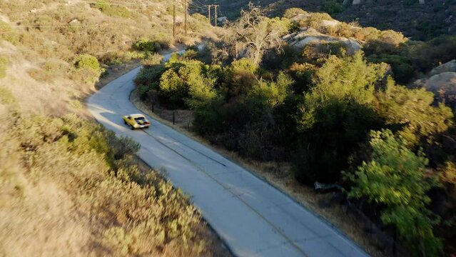 Aerial view following a old, yellow sports car driving on a quiet, curvy mountain road - tilt, drone shot