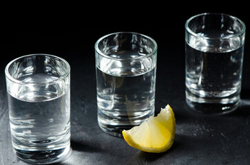 Three glasses of Russian vodka on a black concrete background. Piece of lemon.