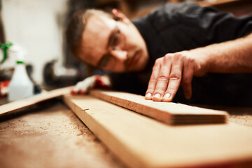 Thats the straightest its going to get. Cropped shot of a focused young male carpenter blowing dust off of a piece of wood after sanding it inside of his workshop during the night.