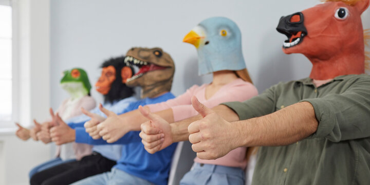 Crazy Eccentric Young People In Trendy Animal Masks Sitting In Row Showing Thumbs Up. Close Up Hands Of Man In Mask Of Horse Sitting On Background Of Other People With Animal Heads. Selective Focus