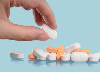 Medical background. Hand holds one of many capsule tablets or pills on blue table. Close up....