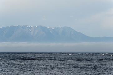View of the surface of the lake from the shore. Small waves, fog in the distance.