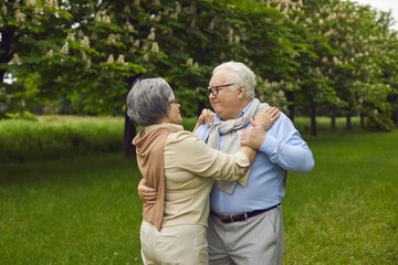 Portrait of happy married senior couple dancing waltz amongst greenery and chestnut trees of beautiful summer park. Two old people in love enjoying each other's company and having good time in nature