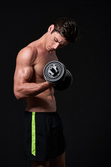 Fototapeta na wymiar One more. Studio shot of a young man working with dumbbells isolated on black.