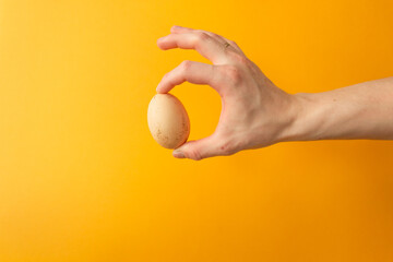Man's hand holding organic raw chicken egg with fingers. Yellow background. Easter holiday concept.