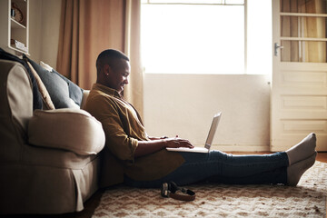 The internet looks fun today. Full length shot of a handsome young man smiling while using a laptop while sitting on the floor in his living room at home.