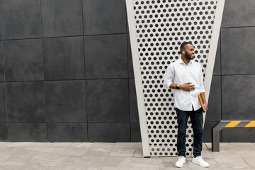 Concentrated stylish business guy wearing casual outfit, using smartphone, chatting with colleague. Handsome serious male freelancer standing outside the office, discussing project with coworker