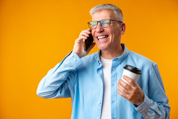 Portrait of happy senior man talking on mobile phone over yellow background