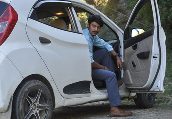 Fototapeta na wymiar A handsome young Indian guy looking sideways while sitting in the car with open door 