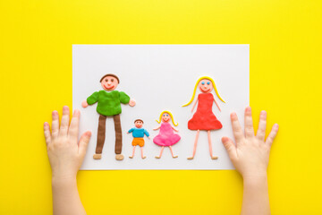Baby hands and human shapes created from colorful modeling clay on white paper. Bright yellow table background. Closeup. Point of view shot. Happy family concept. Top down view.