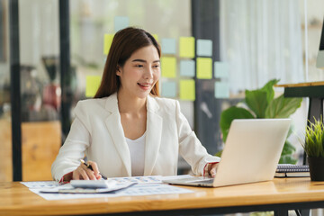 Asian young beautiful joyful woman smiling while working with laptop in office.