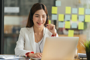 Call center agent with headset working on support hotline in modern office with copy space. Portrait of mature positive agent in conversation with customer over headset looking at camera.