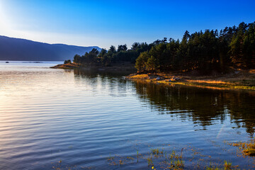 Idyllic mountain landscape at lake with calm water, tree reflection after sunset