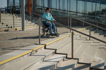 A caucasian woman in a wheelchair cannot go down stairs without a ramp. Hard to access environment. 