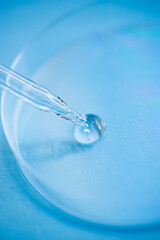 Dropper pipette with serum or cosmetic liquid and petri dish on blue background. Transparent container with liquid and bubbles. The appearance of the texture of the gel. Medicine and beauty concept.