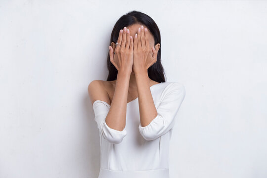 Asian beautiful young woman covers her face with her hands on white background
