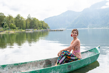 Fototapeta na wymiar Young girl paddling on a wooden boat on a lake near a Bali temple.