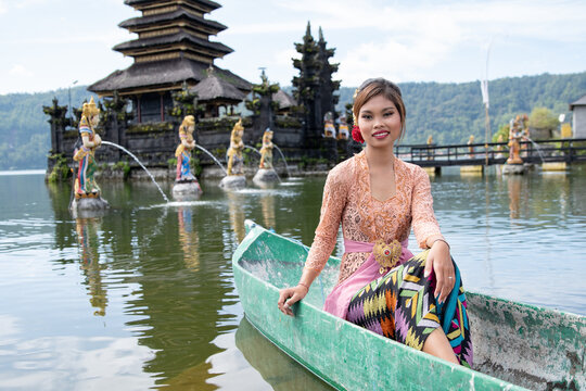 Young girl paddling on a wooden boat on a lake near a Bali temple.