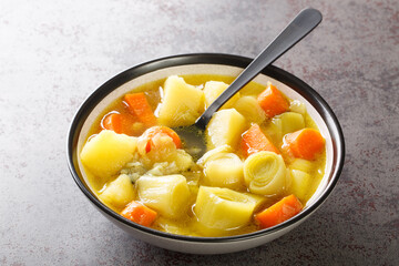 Homemade vegetable soup made from leek, potatoes and carrots close-up in a bowl on a concrete table. horizontal
