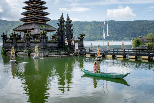 Young girl paddling on a wooden boat on a lake near a Bali temple.