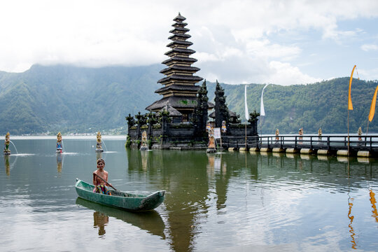 Young girl paddling on a wooden boat on a lake near a Bali temple.