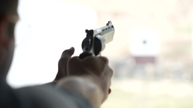 Man shoots with a revolver at targets on the shooting range, close up, blurred focus. Back view of man shooting pistol at target while practicing. Slow motion