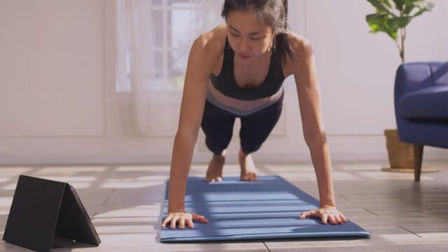 Asian woman in sportswear doing push ups workout exercise on exercise mats at home in the morning.