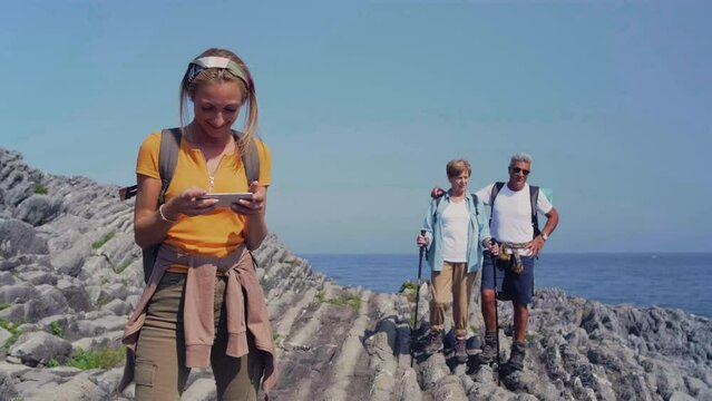 Young woman taking a selfie with a mobile to her parents through flysch rock landscape