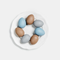 Painted Easter eggs blue, gray, beige colored on round white plate, light background with copy space. Chicken egg pastel shades. Easter holiday food, simple minimal design aesthetic flat lay