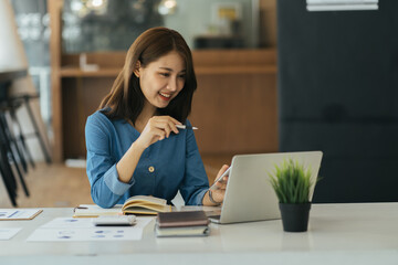 Happy Asian girl sit at desk work on laptop consider read good news in post paper correspondence or letter document, smiling young woman study on computer prepare report.