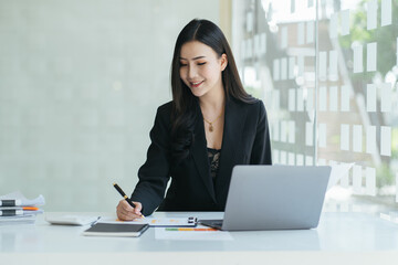 Happy Asian girl sit at desk work on laptop consider read good news in post paper correspondence or letter document, smiling young woman study on computer prepare report.
