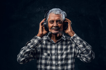 Cheerful old man with headphones dressed in plaid shirt