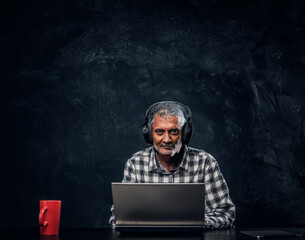 Modern old man with laptop sitting at table against dark background