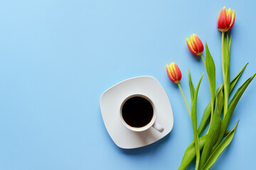 Morning with cup of hot coffee and sweet donuts on blue background. Bouquet of tulips. Top view, copy space, mockup. Flat lay. Food and drinks. Spring holidays. 