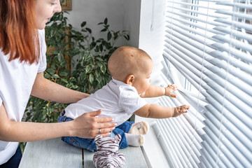 mother and child look out the window. the child grabbed the blinds