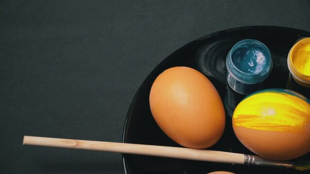 Painted yellow-blue Easter eggs are spinning. Chicken eggs and brushes in the color of Ukraine. Paints, art, sacred eggs, national flag. Lots of fresh raw chicken eggs. Omelette.