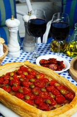 Caramelised onion, cherry tomato and green olive tart, glass of sherry, dish of slice chorizo, and glasses on red wine on villa terrace, Andalusia, Spain.