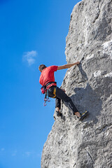 Young male climber climbs on a cliff