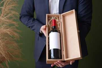 Male hands holding wooden gift box with bottle of red wine.Unrecognizable man offering,advertising alcohol drink on green background