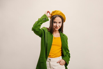 Elegant young caucasian woman in stylish blouse, beret, jacket, posing on white background. Long-haired brunette straightens her headdress. Copy, empty space for text