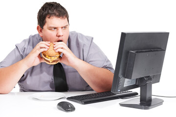 Stop showing me healthy things. A young man eating his lunch at his desk at work while staring with mouth agape at his monitor - unhealthy eating habits.