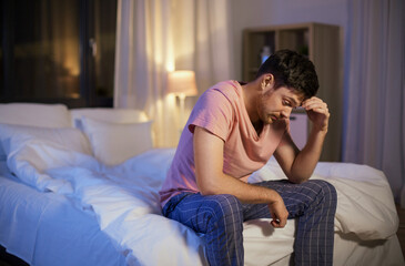 Obraz premium sleep disorder, insomnia and mental health problems concept - unhappy man in pajamas sitting on bed at night