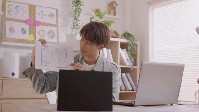 Asian Designer man work from home and communicate with the design team over the internet. On a teblet,women are having a video conference call.